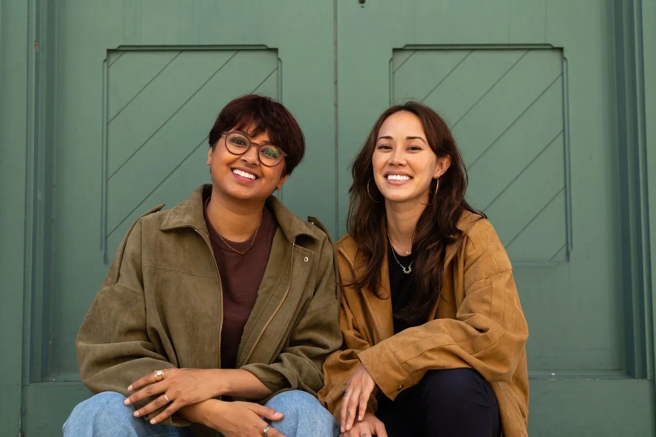 Reservoir’s co-founders, Nabiha Saklayen (left) and Marinna Madrid (right), sitting together in front of a green door.